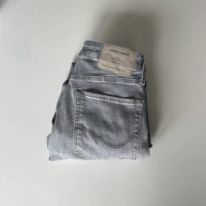 Ljusgrå jeans från Jack & Jones - Snygga ljusgrå jeans från Jack & Jones med klassisk femficksdesign och raka ben. Jeansen har en ljus tvätt och är tillverkade i mjuk denim med en patch i vitt på linningen bak. Perfekta för en avslappnad och trendig stil.
