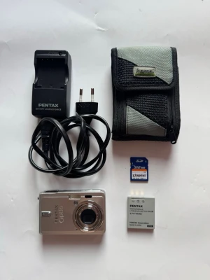 Pentax Optio S6 digitalkamera Kamera Camera Compact Kompakt Mini Digital - Hej,     Det går bra att skicka :)     Säljes: Pentax Optio S6 kompaktkamera inkl batteri + laddare + minneskort + väska     Skick: Bra använt skick. Allting funkar.     Färg: Silver     Info: 100% Äkta, original. Köpt i Sverige.     Produktinfo: Kompakt och stilfull kamera med hela 6 Megapixel upplösning, 2.5 tum stor LCD skärm och 3x optisk zoom.     En kamera perfekt att alltid finnas till hands tack vare storlek och funktion. Välj mellan flera motivanpassade bildprogram, tre olika autofokuse
