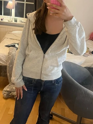 Ljusgrå hoodie med dragkedja - En enkel och stilren ljusgrå hoodie med dragkedja framtill och huva. Hoodien har två fickor fram och ribbade muddar vid ärmslut och nederkant. Perfekt för en avslappnad look och passar till det mesta.