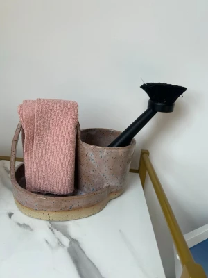 Diskställ  - Säljer en unik handgjord förvaringsbehållare i keramik med handtag. Perfekt för diskborste och trasa i köket. Behållaren är rosa med med prickigt mönster och har två fack, ett större och ett mindre. Snygg och praktisk detalj till diskbänken.ca 20cm bredd ca 16cm hög, OBS trasan o borsten ingår inte 