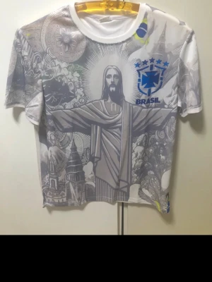 Brasil t-shirt med grafiskt tryck - Unik t-shirt med Brasil-motiv och grafiskt tryck av Kristusstatyn och olika brasilianska symboler. T-shirten är vit med gråa och blå detaljer, har rund hals och korta ärmar. Perfekt för dig som vill sticka ut med en cool och sportig look.