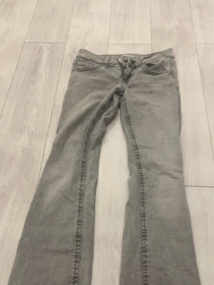 Grå bootcut jeans med låg midja - Snygga grå jeans med bootcut-modell och låg midja. Klassisk femficksdesign och knappgylf. Jeansen har en tvättad look och är tillverkade i ett mjukt denimtyg som ger en avslappnad vibe.