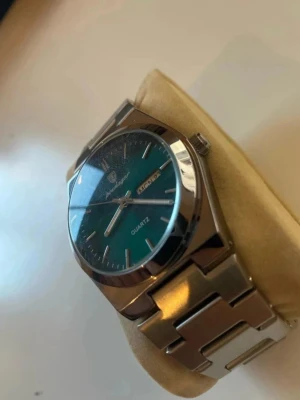 Herrklocka grön urtavla rostfritt stål Quartz - Stilren klocka från Poedagar med grön urtavla och dag/datumvisning. Klockan har en klassisk rund form och en robust länk i silverfärgat metall. Quartz-urverk och tydliga indexmarkeringar gör den både snygg och praktisk. Perfekt accessoar för att lyfta din stil.