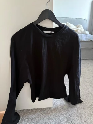 Svart långärmad topp  - En enkel svart långärmad topp med rund halsringning. Tillverkad i mjuk bomull och har en klassisk, normal passform. Perfekt att styla med jeans eller kjol för en clean look.