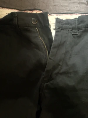 Svarta slim fit chinos Slim/Marco - Säljer ett par svarta chinos i modellen Slim/Marco med slim fit passform. Byxorna har klassisk dragkedja och knapp framtill samt bälteshällor. Perfekta för dig som gillar en smalare siluett och stilren look.