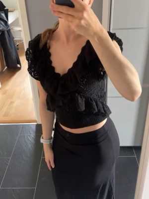 Svart croppad volangblus - Supersöt svart croppad blus med volangdetaljer och djup v-ringning. Blusen är stickad i ett luftigt material och har korta ärmar. 150kr💓