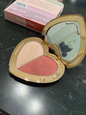 Charlotte Tilbury Love Blush duo - Hjärtformad rouge-duo från Charlotte Tilbury i en lyxig guldförpackning med spegel. Innehåller två nyanser: en ljus beige och en varm rosaröd, båda med pressat hjärtmönster. Perfekt för att skapa en fräsch och naturlig look.