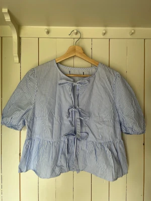 Söt randig topp / blus med knytning  - Denna blus är himla härlig. somrig och söt men kan även vara uppklädd. Den har 3 knyten som du kan öppna. Randig i Blå och Vit. Härliga puffiga armar. Storlek S / M. Vet inte märket tyvärr. Använd 1-2 gånger och behöver bäras mer av ny ägare:)  