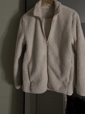 Beige teddyjacka från Intimissimi - Mysig beige teddyjacka från Intimissimi med dragkedja framtill och hög krage. Jackan har en fluffig och mjuk yta som ger en avslappnad och trendig look. Perfekt för att hålla värmen under kyliga dagar.