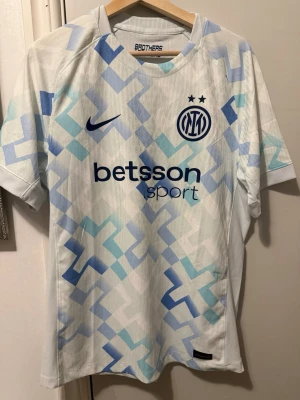 Inter Milan away jersey 2025/2026 authentic  - Snygg Inter Milan bortatröja från Nike i vitt med ljusblått och blått geometriskt mönster. Tröjan har korta ärmar, rund hals och klubbmärke samt Nike-logga på bröstet. Materialet är lätt och andas, perfekt för fotboll eller träning.