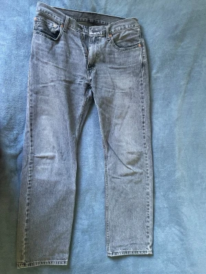 Levi's ljusgrå raka jeans - Säljer ett par klassiska ljusgrå jeans från Levi's med rak passform och fem fickor. Jeansen har en vintage look med Levi's ikoniska läderpatch bak i midjan och röda etiketten på bakfickan. Tillverkade i slitstark denim, perfekta för en avslappnad stil.