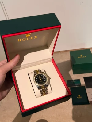 Role klocka i guld och silver - Snygg Role klocka med svart urtavla och tvåfärgad länk i guld och silver. Klockan levereras i originalbox med tillhörande certifikat och manualer. Klassisk design med exklusiv känsla, perfekt för dig som vill sticka ut.