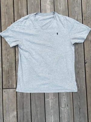Ljusgrå t-shirt från Ralph Lauren - Klassisk ljusgrå t-shirt från Ralph Lauren med liten mörkblå logga broderad på bröstet. T-shirten har rund halsringning och korta ärmar. Tillverkad i mjuk bomull för en skön och avslappnad stil.
