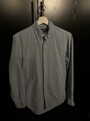 Blå skjorta från Ralph Lauren - Klassisk ljusblå skjorta från Ralph Lauren med button-down krage och broderad logga på bröstet. Modellen är Classic Fit och har långa ärmar. Perfekt till både jeans och chinos för en stilren look.