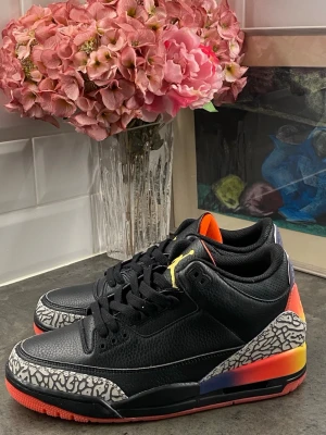 Nike Air Jordan 3 med färgglad häl - Säljer ett par Nike Air Jordan 3 sneakers i svart läder med ikoniskt elefantmönster på tå och häl. Skon har en färgstark gradient på hälen i rött, orange och gult samt svarta snören och röd sula. Perfekt för dig som vill sticka ut med dina sneakers.