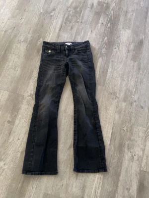 Svarta bootcut jeans med fickdetaljer - Snygga svarta bootcut jeans med klassiska fem fickor och silverknappar på bakfickorna. Jeansen har en lätt utsvängd passform och är tillverkade i ett mjukt denimtyg. Perfekta för en trendig och avslappnad look.