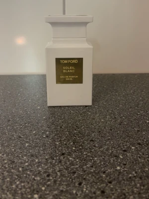 Helt full! Tom Ford Soleil Blanc EdP 100 ml - Helt full Lyxig parfymflaska från Tom Ford i modellen Soleil Blanc. Flaskan är vit med en elegant guldig etikett framtill och har en stilren, fyrkantig form. Innehåller 100 ml Eau de Parfum. Perfekt för dig som gillar exklusiva dofter och snygg design.