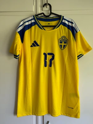 Sverige matchtröja Adidas  - Gul och blå officiell matchtröja från Sveriges landslag med nummer 17 och namnet Gyökeres på ryggen. Tröjan har korta ärmar, broderad landslagssköld och Adidas-logga. Tillverkad i lätt funktionsmaterial som andas.