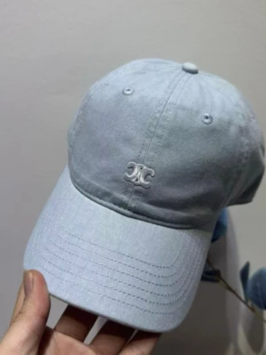 Ljusblå keps från Celine - Snygg ljusblå keps från Celine med broderad logga framtill. Klassisk böjd skärm och justerbar rem bak för perfekt passform. Tillverkad i mjuk bomull som känns skön att bära hela dagen. Perfekt accessoar för en avslappnad och trendig look.
