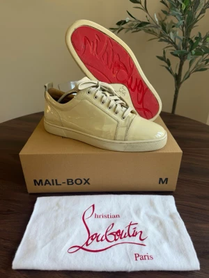  Christian Louboutin - Stilrena off white sneakers i lackläder från Christian Louboutin med klassisk röd sula och vita skosnören. Lågt skaft och minimalistisk design som ger en lyxig känsla. Perfekta för dig som vill sticka ut med exklusiva detaljer och hög modegrad.