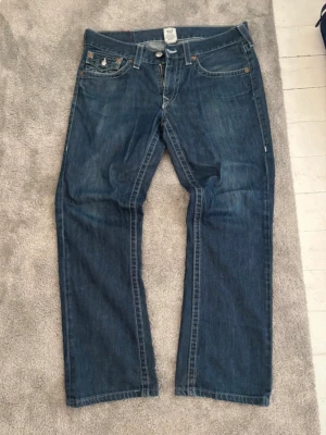 True Religion Jeans - Säljer dessa snygga True Religion Jeans med lite bootcut. Knappt använda, inga skador eller liknande.   Midja: 48cm Ytterbenslängd: 101cm