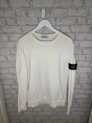 Stone Island tröja - Stone Island crewneck i vit färg. Väldigt clean och stilren modell med badge på armen. Endast ett litet diskret hål på nedre baksidan vid sidan (se bild), annars i mycket bra skick.