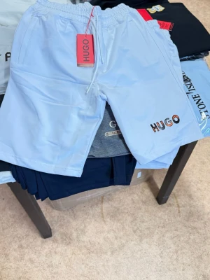 Shorts från HUGO BOSS - Snygga ljusblå shorts från HUGO med elastisk midja och snörning. Logotypen är broderad i flera färger på ena benet. Perfekta för sommarens alla aktiviteter och har en avslappnad passform.