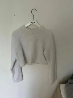 Vit fluffig stickad tröja H&M - Mysig vit stickad tröja från H&M i storlek XS. Tröjan är fluffig med rund halsringning och har en croppad passform. Perfekt för dig som gillar en enkel men trendig look. Materialet känns mjukt och behagligt mot huden.