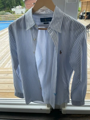 Blårandig skjorta från Ralph Lauren - Klassisk blårandig skjorta från Ralph Lauren med lång ärm och knappar framtill. Skjortan har en broderad logga på bröstet och är tillverkad i mjuk bomull. Perfekt för en stilren och avslappnad look. Ny pris 1750 säljer för 1000 pris kan diskuteras. Helt ny har inte använt på grund av att den va för liten
