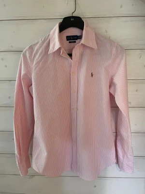 Ralph Lauren skjorta  - Klassisk skjorta från Ralph Lauren i rosa och vitt med tunna ränder. Skjortan är i jätte bra skick/nytt skick.                                                                      Skriv gärna om ni har några frågor!
