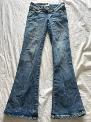 Blå bootcut jeans med låg midja - Säljer ett par klassiska blå bootcut jeans med låg midja och utsvängda ben. Jeansen har fem fickor och är gjorda i denim med snygg tvätt. Perfekta för dig som gillar retrostil och vill ha ett par jeans som sticker ut.