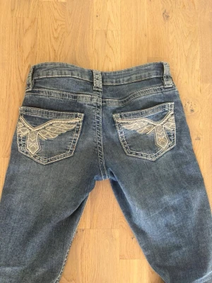 Blå bootcut jeans med vingar på  - Säljer ett par blå bootcut jeans från Ginatricot! Inga tecken på användning. Storlek 158.