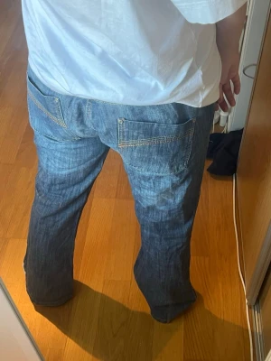 Blå bootcut/wide jeans - Säljer ett par blå bootcut/wide jeans. Jeansen har klassiska bakfickor med synliga sömmar och är tillverkade i bomull. Perfekta för en avslappnad och trendig stil.