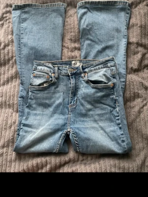Blå bootcut jeans från 157 - Säljer ett par ljusblå bootcut jeans från 157 med klassisk femficksdesign och hög midja. Jeansen har en snygg tvättad look och breda ben som ger en retrovibe. Tillverkade i denim med kontrastsömmar och metallknappar.