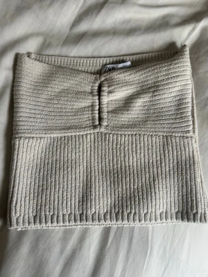 Beige ribbad tubtopp från Zara - Trendig stickad beige tubtopp från Zara i ribbat material. Toppen har en snygg detalj framtill och är croppad i modellen🌸Storlek på toppen är M, men jag skulle säga att den passar s/xs beroende på byststorlek 