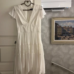 Vit spetsklänning med volang - Vit asymmetriskt klänning från asos. Passar perfekt till både student och sommar. Endast använd 2 gånger✨