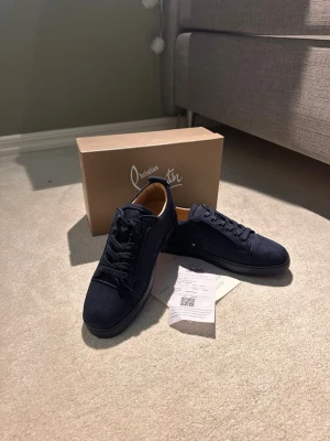 Mörkblå sneakers från Christian Louboutin - Snygga mörkblå sneakers från Christian Louboutin i mocka med matchande mörkblå sula och diskret logga på hälen. Klassisk låg modell med svarta skosnören och stilren design som passar till det mesta.