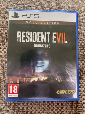 Resident Evil 7 biohazard Gold PS5 - Resident Evil 7 biohazard Gold Edition till PS5. Skräckspel där du utforskar ett övergivet hus och möter läskiga fiender. Innehåller extra DLC som End of Zoe och Banned Footage. Omslaget är svart med skrämmande motiv och spelet är i blå plastfodral.