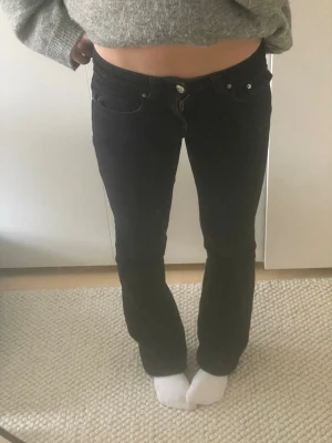 Svarta bootcut jeans med låg midja - Säljer ett par svarta bootcut jeans med låg midja och klassisk femficksdesign. Jeansen har raka ben som går ut lite nedtill och stängs med knapp och dragkedja. Perfekta för en avslappnad och trendig look.