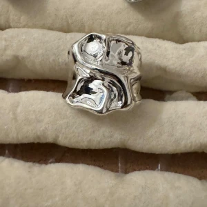 Chunky silverfärgad statementring - Säljer en chunky ring i silverfärgad med organisk, vågig form och blank finish. Ringen har en modern och unik design som verkligen sticker ut. Perfekt för dig som gillar att bära smycken som syns och ger en cool touch till din stil.