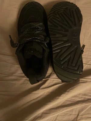 Svarta skor från UGG - Säljer ett par svarta kängor från UGG med grov sula och snörning. Skorna har en sportig look med robust yttersula och detaljerade sömmar. Perfekta för dig som vill ha både stil och funktion i höst och vinter. Storlek 36, använt 1 gång