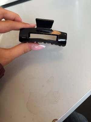 Svart hårklämma i plast - Snygg svart hårklämma i glansig plast med rektangulär form och öppet mittparti. Perfekt för att snabbt sätta upp håret i en trendig look. Klämman har stark fjäder och greppvänliga taggar.