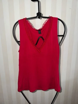 Röd linnetopp med spetsdetalj - Snygg röd linnetopp från Mango med v-ringning och spetsdetalj vid halsen. Toppen är ärmlös och har en enkel, slim passform som är perfekt för att skapa en cool och avslappnad look. Materialet känns mjukt och lätt mot huden.