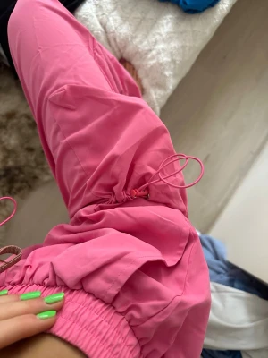 Rosa cargobyxor med fickor - Säljer ett par coola rosa cargobyxor med elastisk midja och snörning vid benslut. Byxorna har stora sidofickor och är tillverkade i ett lätt material som känns skönt att bära. Aldrig använda. FRAKT INGÅR