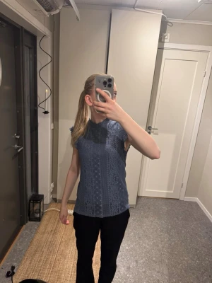 Blå spetsblus med volangärmar - Söt blå blus med spetsdetaljer och små volangärmar. Toppen har en lätt v-ringad hals och är ärmlös, vilket ger en luftig känsla. Perfekt för dig som gillar romantiska detaljer och vill ha något som sticker ut lite extra.