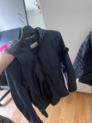  Stone Island windbracker  - Snygg marinblå vindjacka från Stone Island med huva och dragkedja framtill. Jackan har den klassiska logotypen på ärmen och två fickor med knappstängning. Perfekt nu under våren - hösten. Storlek junior, men passar storlek S skulle jag säga. ( nypris oklart )