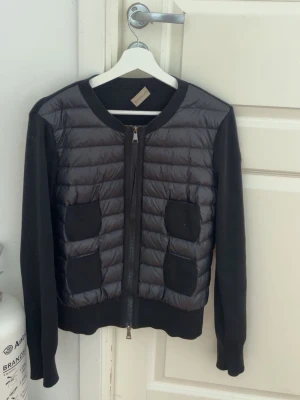 Svart cardiganjacka från Moncler - Snygg svart cardiganjacka från Moncler med quiltad framsida och två fickor. Ärmar och rygg i mjukt stickat material, framstycke i glansig nylon. Rund halsringning och dragkedja framtill. Säljer då den inte kommer till användning längre. Storlek M men passar mig som har S. Lappen sitter har lossnat på ena sidan vilket syns på bild 3. Kvitto och lappar finns. 💞