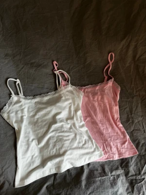 Två linnen med spetskant - Säljer två linnen med tunna axelband och spetskant upptill. Ett är vitt och det andra är ljusrosa. Båda är i mjukt, stretchigt material.