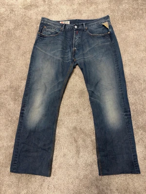 Blå raka jeans från Replay - Längd: 105cm                                              Midjebredd: 47,5cm                                 Benöppning: 24,5cm                                          Snygga blå jeans från Replay med raka ben och klassisk femficksdesign. Jeansen har slitningar och ljusare partier på låren för en cool, avslappnad look. Tillverkade i denim med detaljerade sömmar och läderpatch bak i midjan.
