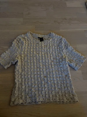 Vit strukturerad topp från Lindex - Supersnygg vit topp från Lindex i storlek S. Toppen har korta ärmar och ett unikt, strukturerat tyg med rynkade detaljer som ger en cool och trendig look. Perfekt att styla med jeans eller kjol för en fräsch outfit.